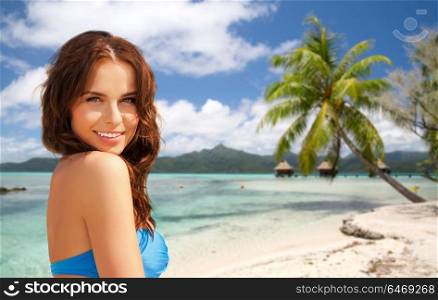 summer holidays, vacation and travel concept - happy young woman posing in bikini swimsuit over exotic tropical beach with bungalow sheds background. happy woman in bikini swimsuit on tropical beach
