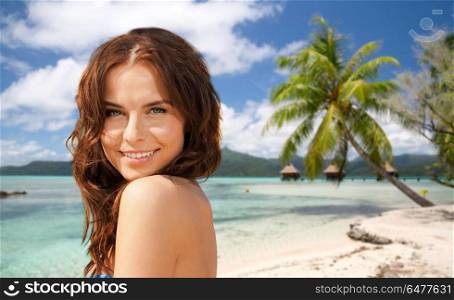 summer holidays, vacation and travel concept - happy young woman posing in bikini swimsuit over exotic tropical beach with bungalow sheds background in french polynesia. happy woman in bikini swimsuit on tropical beach. happy woman in bikini swimsuit on tropical beach