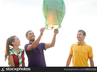 summer holidays, vacation, celebration and people concept - group happy friends with chinese sky lantern on beach