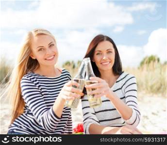 summer holidays, vacation, celebration and people concept - happy teenage girls or young women drinking beer or lemonade on beach