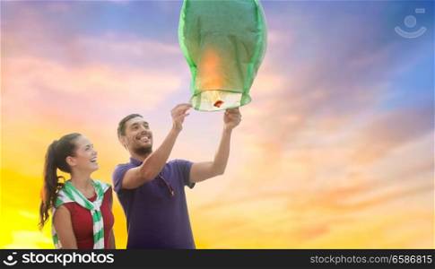 summer holidays, vacation, celebration and people concept - happy young couple launching chinese sky lantern in the evening. happy couple launching chinese sky lantern