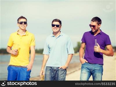 summer, holidays, vacation, happy people concept - group of friends having fun on the beach with bottles of beer or non-alcoholic drinks