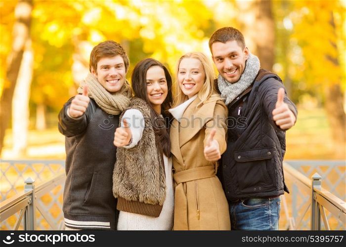 summer, holidays, vacation, happy people concept - group of friends or couples having fun and showing thumbs up in autumn park