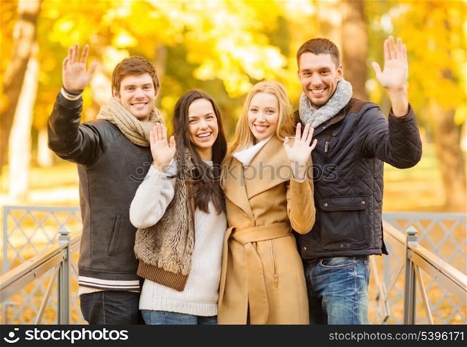summer, holidays, vacation, happy people concept - group of friends or couples having fun and waving hands in autumn park