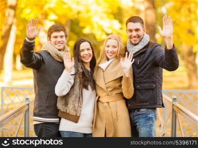 summer, holidays, vacation, happy people concept - group of friends or couples having fun and waving hands in autumn park