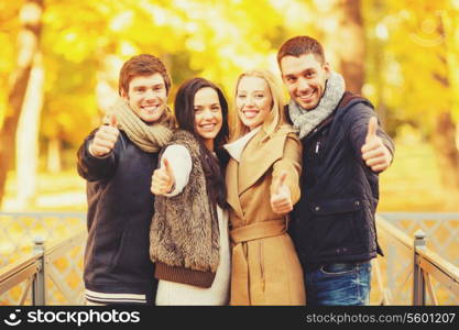 summer, holidays, vacation, happy people concept - group of friends or couples having fun and showing thumbs up in autumn park