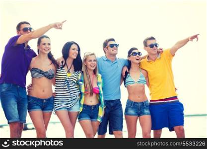 summer, holidays, vacation, happy people concept - group of friends pointing somewhere on the beach