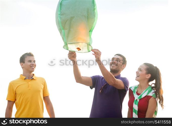 summer, holidays, vacation, happy people concept - group of friends with chinese sky lanterns on the beach