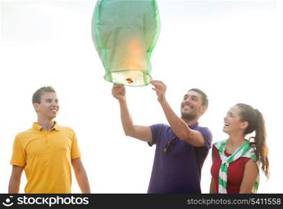 summer, holidays, vacation, happy people concept - group of friends with chinese sky lanterns on the beach