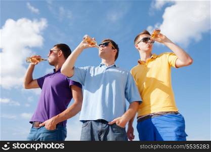 summer, holidays, vacation, happy people concept - group of male friends having fun on beach with bottles of beer or non-alcoholic drinks