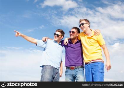 summer, holidays, vacation, happy people concept - group of male friends walking on the beach pointing finger somewhere