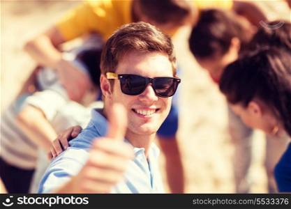 summer, holidays, vacation, happy people concept - man with group of friends on the beach showing thumbs up