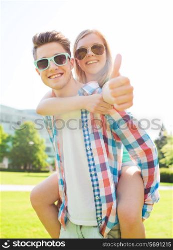 summer holidays, vacation, love, gesture and friendship concept - smiling teen couple in sunglasses having fun and showing thumbs up in park