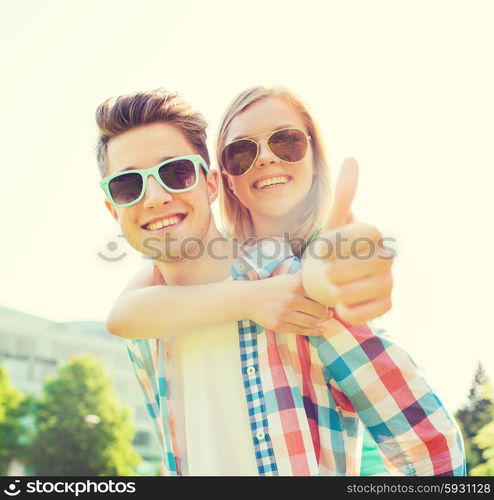 summer holidays, vacation, love, gesture and friendship concept - smiling teen couple in sunglasses having fun and showing thumbs up in park