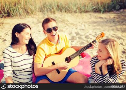 summer holidays, vacation, music, happy people concept - group of friends with guitar having fun on the beach