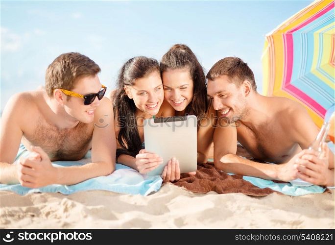 summer, holidays, vacation, technology and happy people concept - group of smiling people with tablet pc under umbrella on the beach