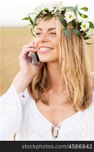 summer holidays, vacation, technology and people concept - close up of smiling young woman in wreath of flowers calling on smartphone at countryside