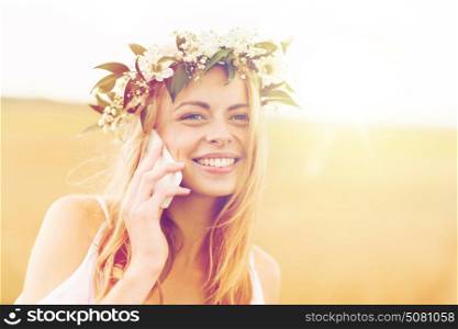 summer holidays, vacation, technology and people concept - close up of smiling young woman in wreath of flowers calling on smartphone at countryside. happy young woman calling on smartphone at country