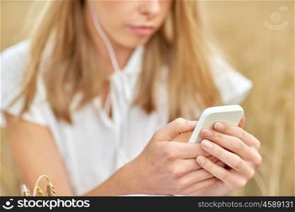 summer holidays, vacation, technology and people concept - close up of young woman in white dress with smartphone and earphones listening to music on cereal field