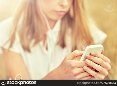 summer holidays, vacation, technology and people concept - close up of young woman in white dress with smartphone and earphones listening to music on cereal field. close up of woman with smartphone and earphones