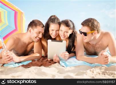 summer holidays, vacation, technology and people concept - group of happy friends with tablet pc computer sunbathing on beach