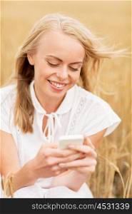 summer holidays, vacation, technology and people concept - smiling young woman in white dress with smartphone on cereal field