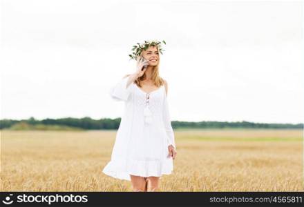 summer holidays, vacation, technology and people concept - smiling young woman in wreath of flowers calling on smartphone on cereal field