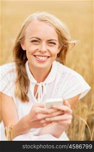 summer holidays, vacation, technology and people concept - smiling young woman in white dress with smartphone and earphones listening to music on cereal field