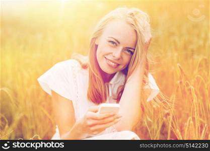 summer holidays, vacation, technology and people concept - smiling young woman in white dress with smartphone on cereal field. happy young woman with smartphone on cereal field