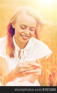 summer holidays, vacation, technology and people concept - smiling young woman in white dress with smartphone on cereal field. happy young woman with smartphone on cereal field