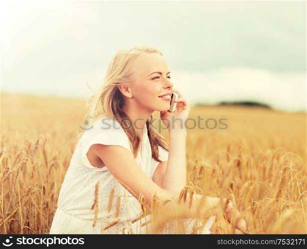 summer holidays, vacation, technology and people concept - smiling young woman in white dress calling on smartphone on cereal field. happy young woman calling on smartphone at country
