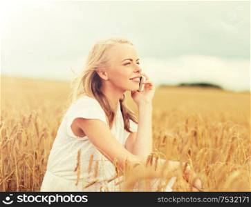 summer holidays, vacation, technology and people concept - smiling young woman in white dress calling on smartphone on cereal field. happy young woman calling on smartphone at country