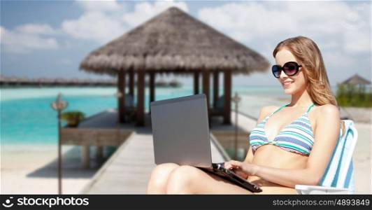 summer holidays, vacation, technology, people and internet - happy young woman in shades with laptop computer over exotic tropical beach and bungalow shed background