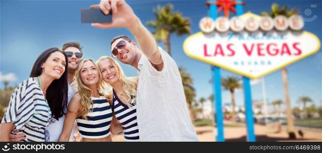 summer holidays, vacation, tourism and travel concept - group of smiling friends in striped clothes taking selfie by smartphone over welcome to fabulous las vegas sign background. friends travelling to las vegas and taking selfie