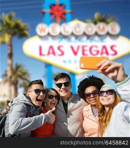summer holidays, vacation, tourism and travel concept - group of smiling teenage friends taking selfie by smartphone over welcome to fabulous las vegas sign background. friends travelling to las vegas and taking selfie