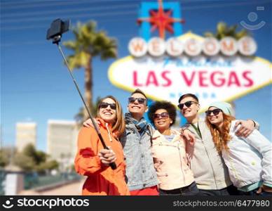 summer holidays, vacation, tourism and travel concept - group of smiling teenage friends taking picture by smartphone selfie stick over welcome to fabulous las vegas sign background. friends travelling to las vegas and taking selfie. friends travelling to las vegas and taking selfie