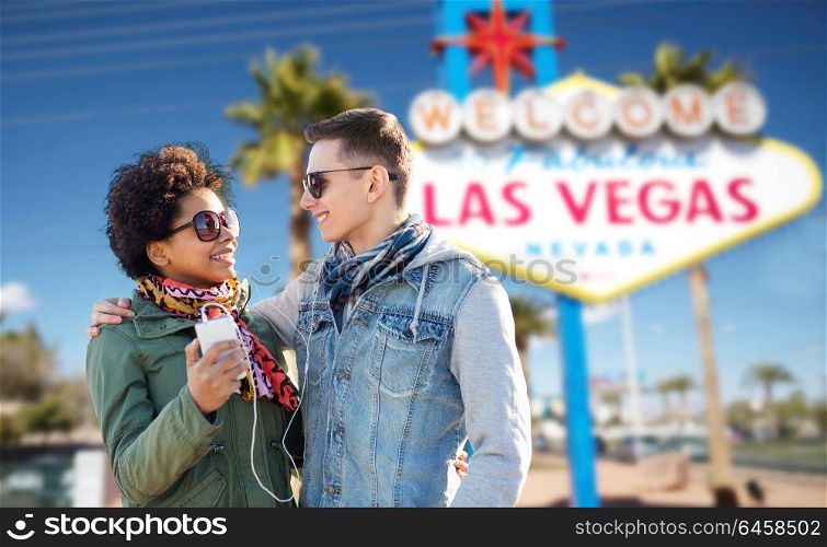summer holidays, vacation, tourism and travel concept - smiling couple with smartphone and earphones listening to music over welcome to fabulous las vegas sign background. couple with smartphone and earphones at las vegas