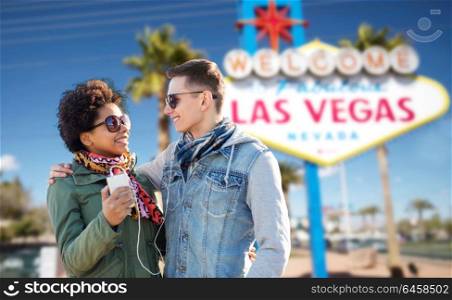 summer holidays, vacation, tourism and travel concept - smiling couple with smartphone and earphones listening to music over welcome to fabulous las vegas sign background. couple with smartphone and earphones at las vegas