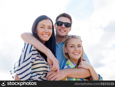 summer holidays, vacation, tourism, travel and people concept - group of happy friends hugging over sky background