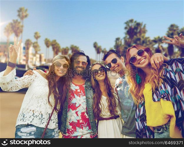 summer holidays, vacation, travel and people concept - smiling young hippie friends showing peace hand sign over venice beach in los angeles background. hippie friends showing peace over venice beach