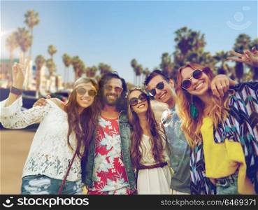 summer holidays, vacation, travel and people concept - smiling young hippie friends showing peace hand sign over venice beach in los angeles background. hippie friends showing peace over venice beach