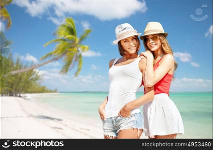 summer holidays, vacation, travel and people concept - smiling young women in hats and casual clothes over exotic tropical beach with palm trees background. smiling young women in hats on beach