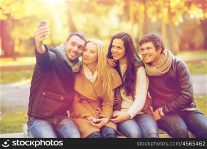 summer, holidays, vacation, travel and tourism concept - group of friends or couples having fun with smartphone photo camera in autumn park