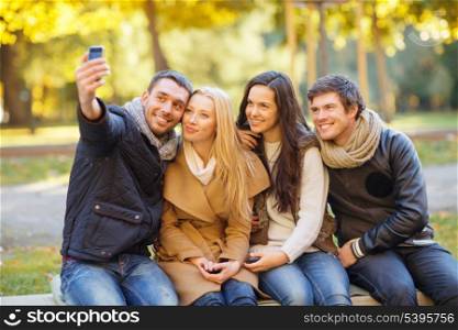 summer, holidays, vacation, travel and tourism concept - group of friends or couples having fun with smartphone photo camera in autumn park