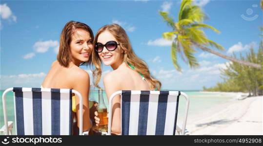 summer holidays, vacation, travel and tourism people concept - smiling young women with drinks sunbathing over exotic tropical beach with palm trees and sea shore background. happy young women with drinks sunbathing on beach