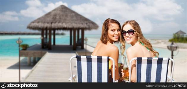 summer holidays, vacation, travel and tourism people concept - smiling young women with drinks sunbathing over exotic tropical beach and bungalow background. happy young women with drinks sunbathing on beach