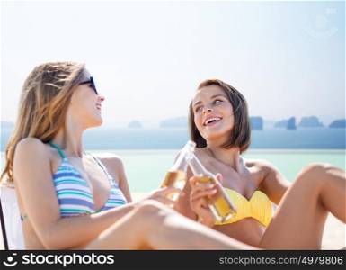 summer holidays, vacation, travel and tourism people concept - smiling young women with drinks sunbathing over sea and infinity edge pool background. happy young women with drinks sunbathing on beach