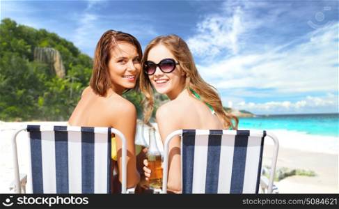 summer holidays, vacation, travel and tourism people concept - smiling young women with drinks sunbathing on folding chairs over exotic tropical beach background. happy young women with drinks sunbathing on beach. happy young women with drinks sunbathing on beach