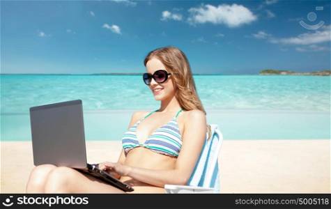 summer holidays, vacation, travel, technology and people concept - smiling women in sunglasses with laptop computer sunbathing in lounge over exotic tropical beach background. woman with laptop sunbathing in lounge on beach