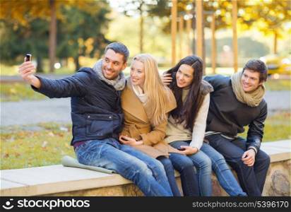 summer, holidays, vacation, travel, tourism concept - group of friends or couples having fun with smartphone photo camera in autumn park